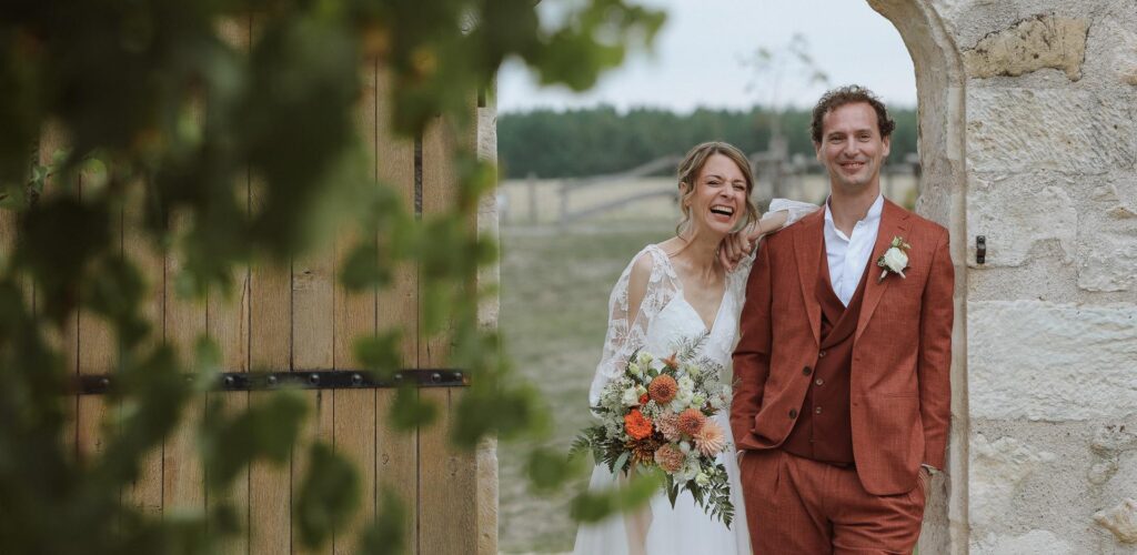 Mariés riant sous une arche en pierre lors de leur mariage en Touraine, organisé par Épure Event