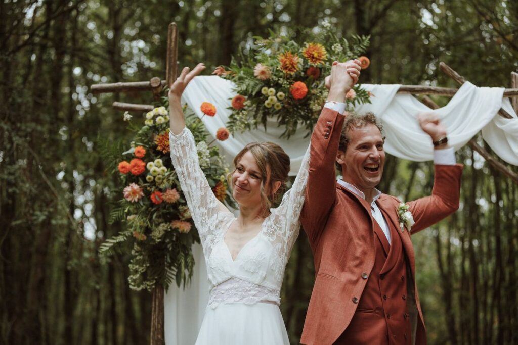 Les mariés lèvent les bras à la fin de leur cérémonie laïque en forêt, mariage en Touraine